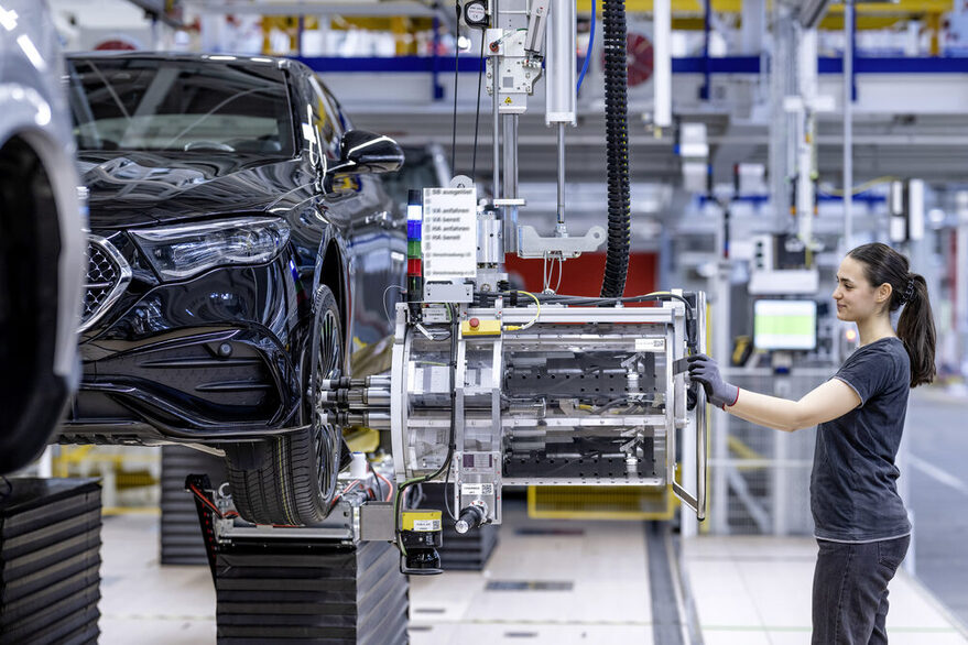 Eine Monteurin montiert in einer Autofabrik einen Reifen an ein Fahrzeug.