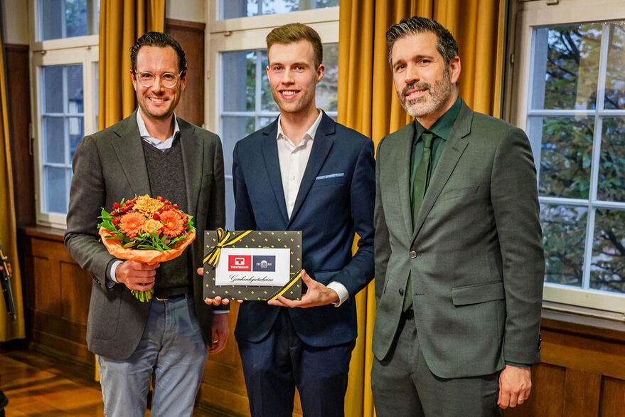 Erster Bürgermeister Dr. Fabian Mayer mit Blumestrauß,Bezirksvorsteher Nick Gumenick hält ein Geschenk in der Hand, Bezirksbeirat Christian Musse steht daneben.