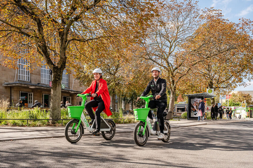 Ein Mann und eine Frau fahren bei schönem Herbstwetter vor dem Cannstatter Bahnhof mit einem Fahrrad des Anbieters Lime.