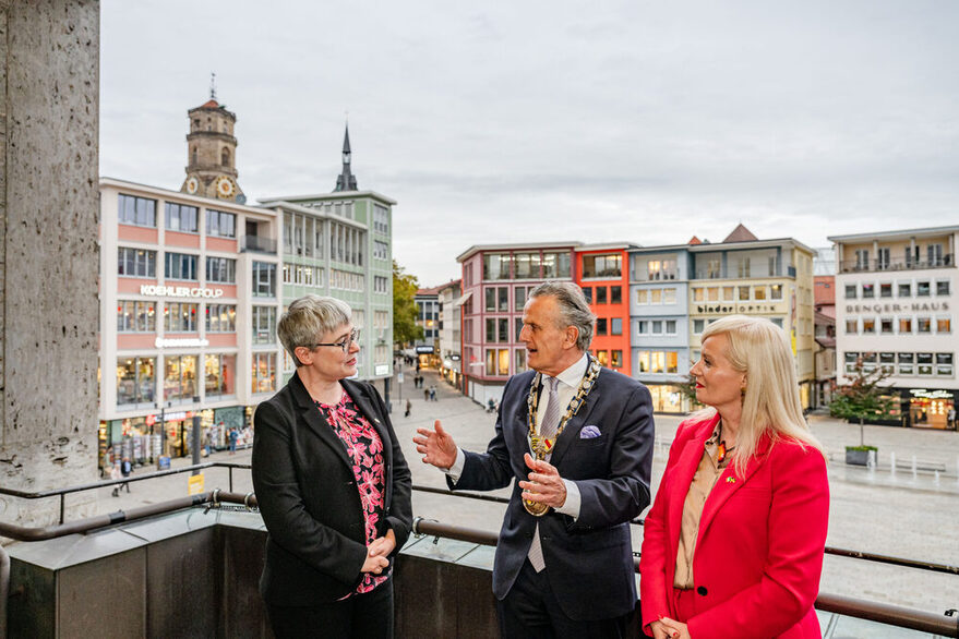Zwei Frauen und ein Mann stehen auf dem Balkon des Rathauses und unterhalten sich.