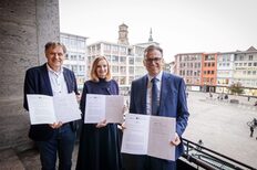 The Mayor for Youth and Education, Isabel Fezer (center), Dr. Joachim Bläse (right), District Administrator of Ostalbkreis, and Richard Arnold (left), Lord Mayor of Schwäbisch Gmünd, hold the cooperation agreement in their hands on the balcony of Stuttgart City Hall.