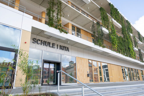 Zu sehen sind der Eingangsbereich des Gebäudes sowie die Begrünung an den Balkonen.