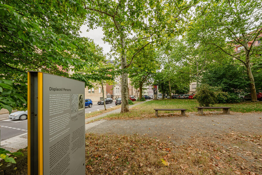Ein Platz umgeben von Bäumen in Stuttgart-West mit einer Erinnerungsstele im Vordergrund.
