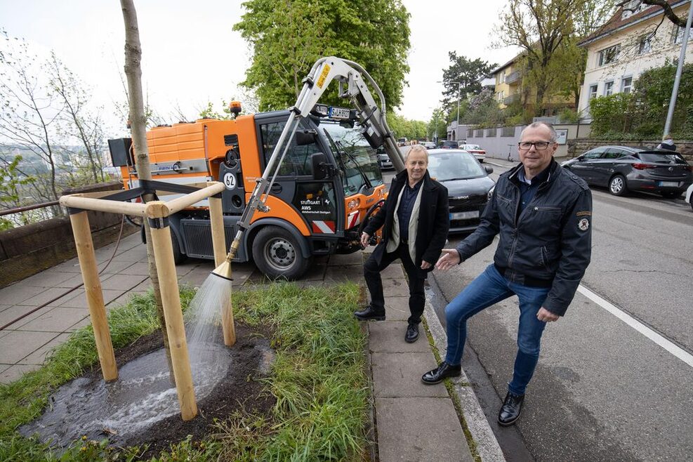 Bürgermeister für das technische Referat, Dirk Thürnau, und der Leiter des Garten-, Friedhofs- und Forstamts, Volker Schirner, neben einem Gießfahrzeug der Stadt, das gerade einen Baum bewässert.