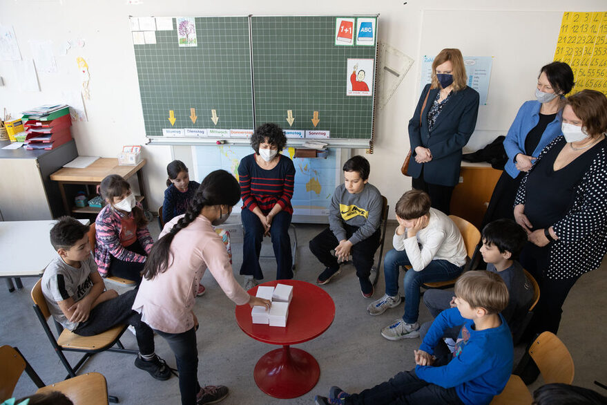 Kinder spielen im Klassenzimmer, Bürgermeisterin Fezer, Ministerin Theresa Schopper und Regierungspräsidentin Susanne Bay schauen zu. r