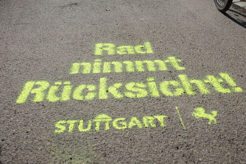 Auf dem Asphalt steht mit Sprühkreide geschrieben: Rad nimmt Rücksicht und das Logo der Stadt Stuttgart