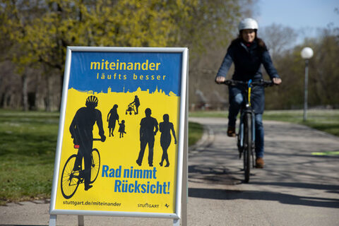 Plakat mit Aufschrift: Rad nimmt Rücksciht, Miteinander läufts besser, im Hintergrund nähert sich eine Radfahrerin.