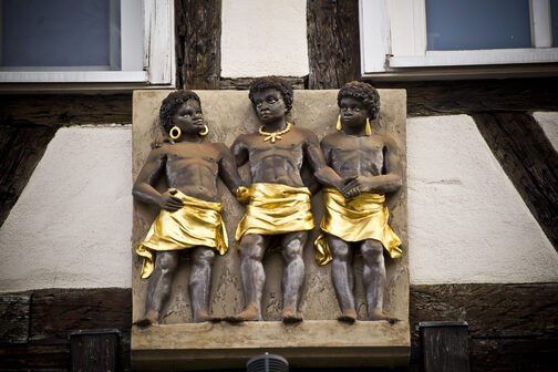 Das Relief "Drei Mohren" zeigt dei schwarze Menschen, die mit goldenem Schmuck und ebenfalls goldenen Wickelröcken nebeneinander stehen und sich brüderlich die Hand reichen.