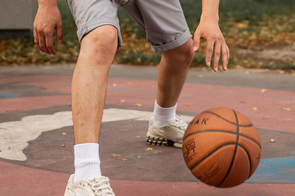 Auf einem Basketballfeld sind zwei Beine und ein Basketball zu sehen.
