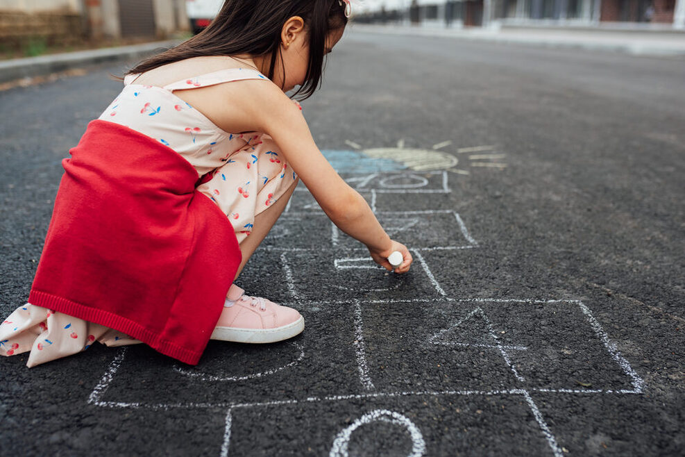 Ein kleines Mädchen malt auf einer Straße mit Straßenmalkreide