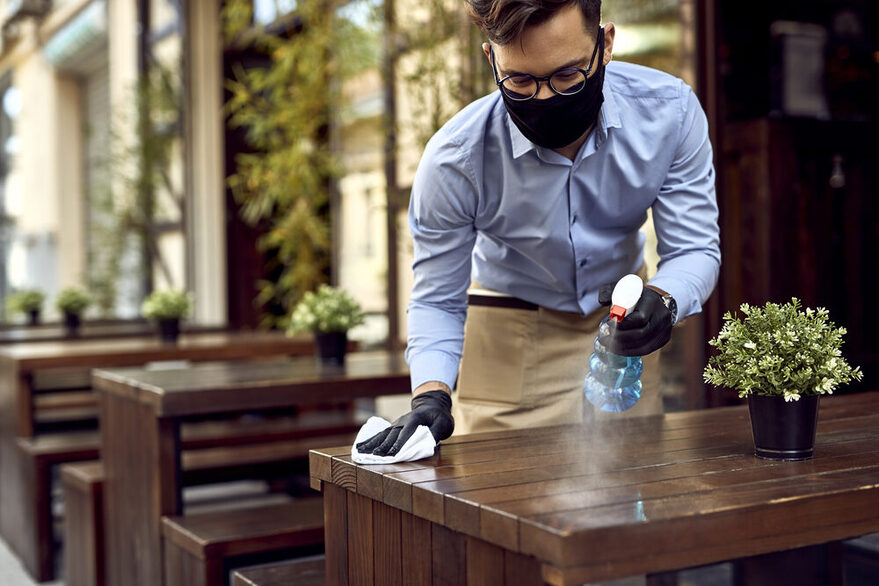 Mann putzt einen Tisch mit Desinfektionsmittel vor einem Restaurant