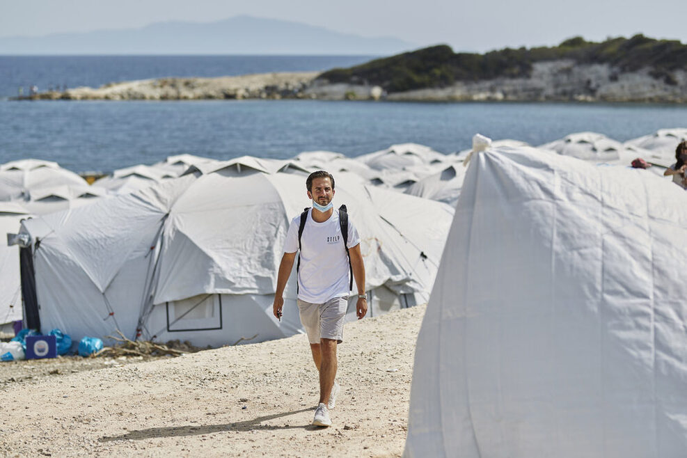Serkan Eren läuft durch eine weiße Zeltstadt an einem Strand in Griechenland.
