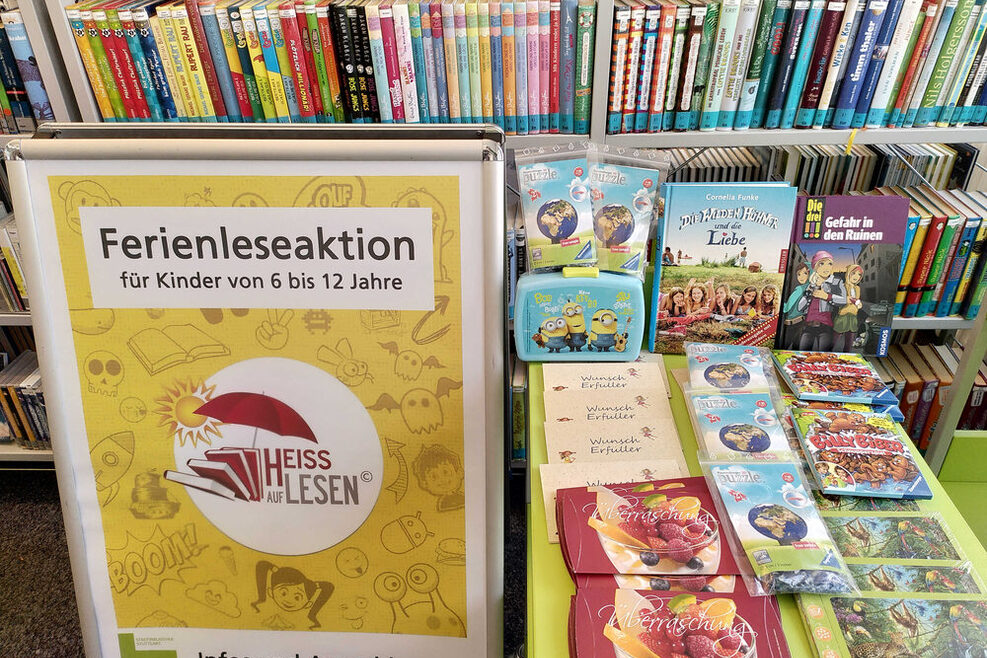 Mehrere Dutzend Bücher für Kinder und Jugendliche liegen in der Stadtteilbibliothek Bad-Cannstatt aus. Im linken vorderen Bildbereich ist zudem ein Aufsteller zu sehen, der die Ferienleseaktion für Kinder von 6 bis 12 Jahren "Heiß auf Lesen" bewirbt.