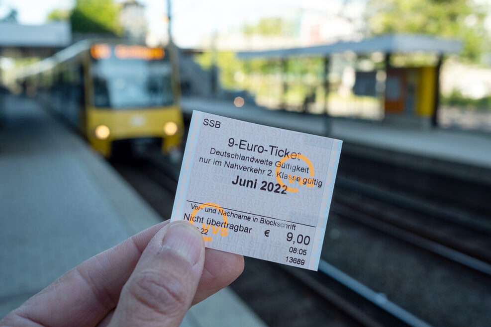 Eine Hand hält an einem U-Bahn-Bahnsteig ein 9-Euro-Ticket in die Höhe