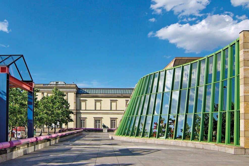 Neue Staatsgalerie mit geschwungener Travertin-Fassade, mit pinken und blauen Handläufen an den Treppen sowie grünen Stahlträgern.