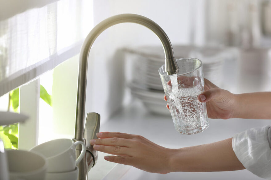 Frau füllt Wasserglas mit Leitungswasser in der Küche