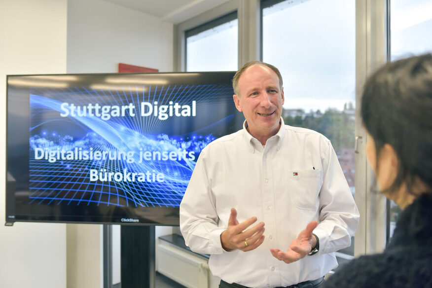 Thomas Boenig im Gespräch mit Interviewprtnerin, im Hintergrund ist ein Bildschirm zu sehen mit Aufschrift: Stuttgart digital, Digitalisierung jenseits der Bürokratie.