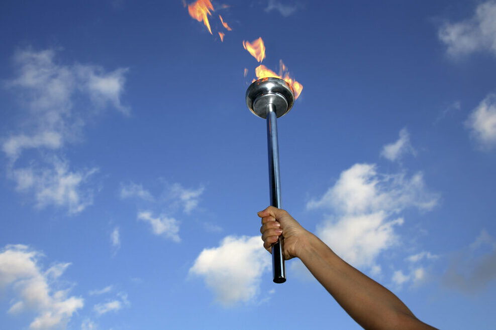 Die olympische Flamme vor blauem Himmel.