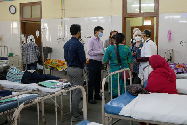 Menschen stehen im Krankenzimmer mit Bette und Patienten