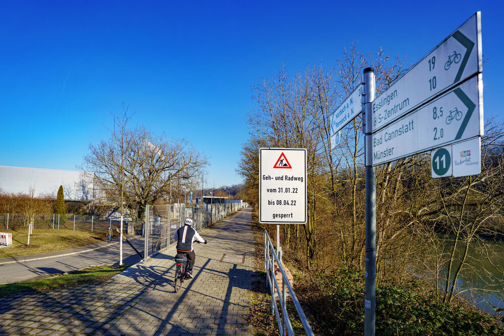 Ein Radfahrer fährt auf dem Neckarradweg, ein Schild weist auf die Sperrung ab dem 31. Januar hin.