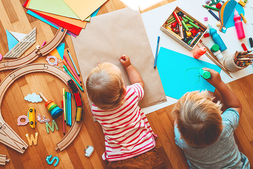 Zwei Kinder malen auf dem Boden liegend auf Papier mit Buntstiften in einer Kindertagesstätte.