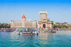 Bunte Schiffe auf blauem. Im Hintergrund ist das Hotel Taj Mahal Palace and der Triumphbogen Gateway of India