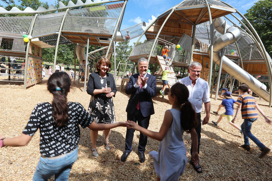 Kinder spielen und tanzen auf dem Spielplatz: Finanzstaatssekretärin Gisela Splett und Oberbürgermeister Dr. Frank Nopper klatschen in die Hände.