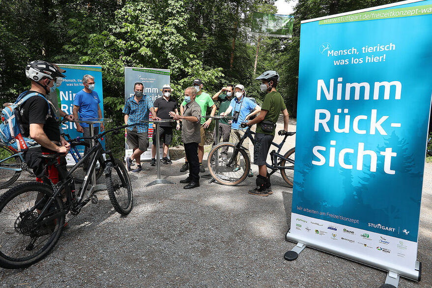An Stehtischen hinter denen Banner zum Freizeitkonzept zu sehen sind, informieren Teilnehmer des Planungsprozesses Waldbesucher, wie hier Fahrradfahrer.