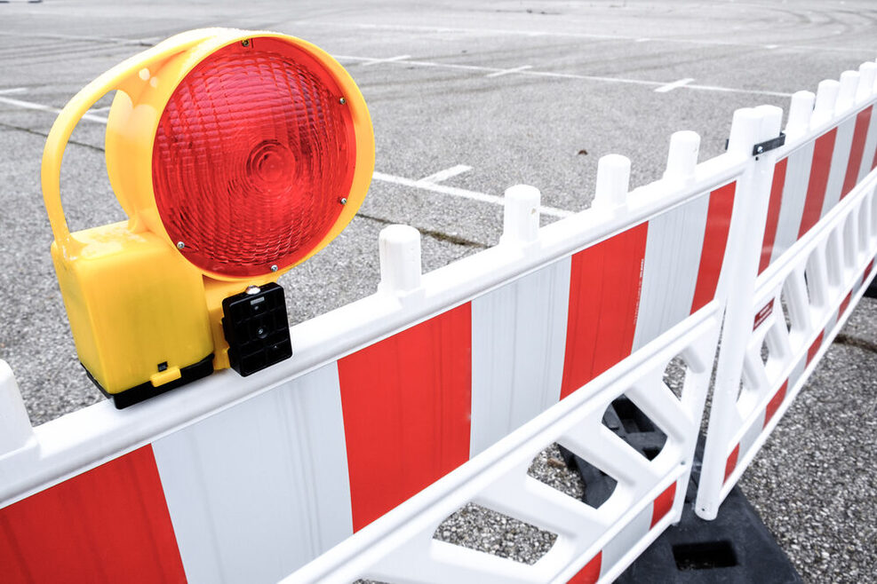 Eine rot-weiß gestreifte Sicherheitsabsperrung steht auf einer Straße. Auf ihr ist ein rotes Baulicht montiert.