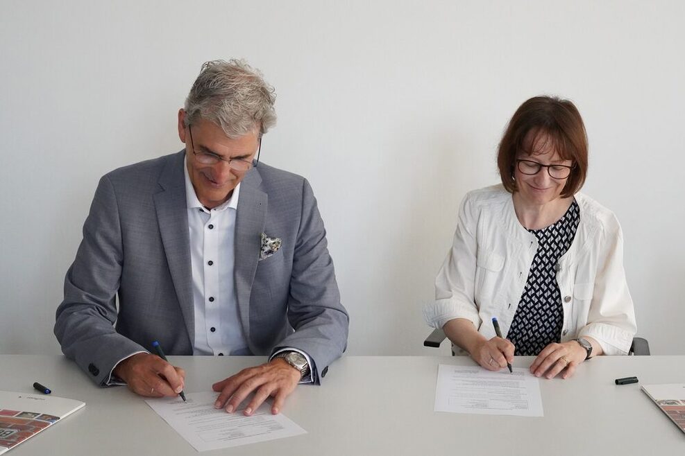 Réné Wollnitz und Dr. Katharina Ernst unterzeichnen den Vertrag an einem Schreibtisch.