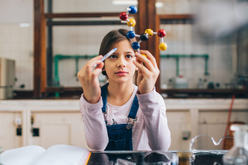 Ein junges Mädchen arbeitet in einem Klassenzimmer an einem Modell eines Moleküls.