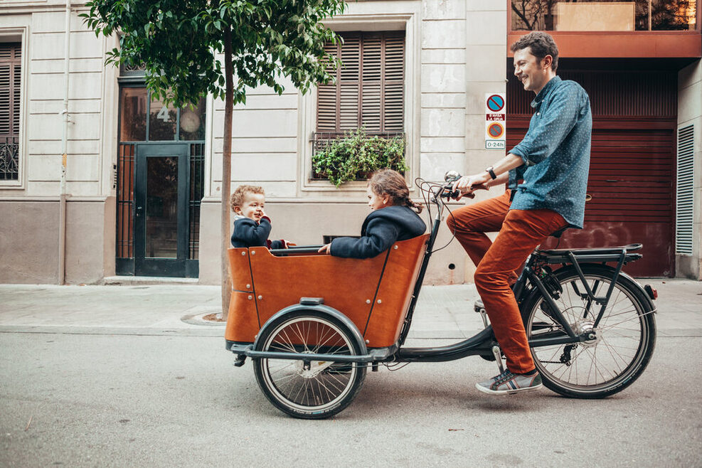 Ein Vater fährt mit seinen zwei Kindern mit dem Lastenrad