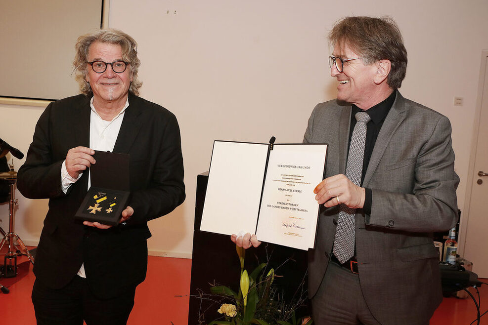 Axel Clesle zegt die Schatulle mit dem Orden, rechts neben ihm steht Minister Manfred Lucha. Er hält die Verleihungsurkunde in Händen.