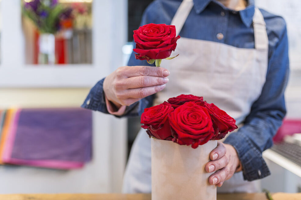 Frau steckt rote Rosen in eine Vase.
