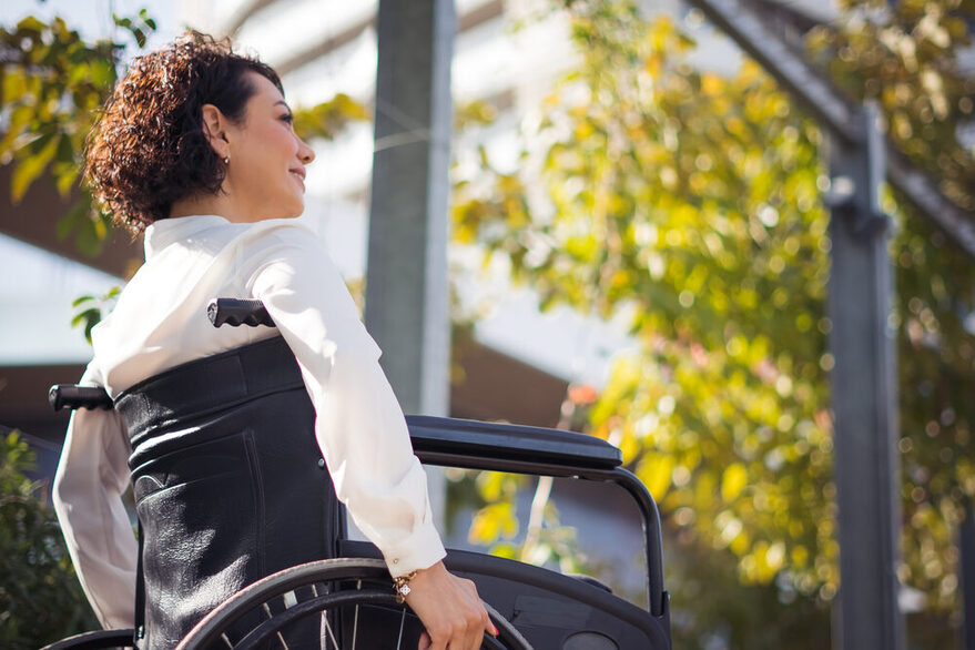 Eine Frau mit weißer Bluse sitzt in einem Rollstuhl