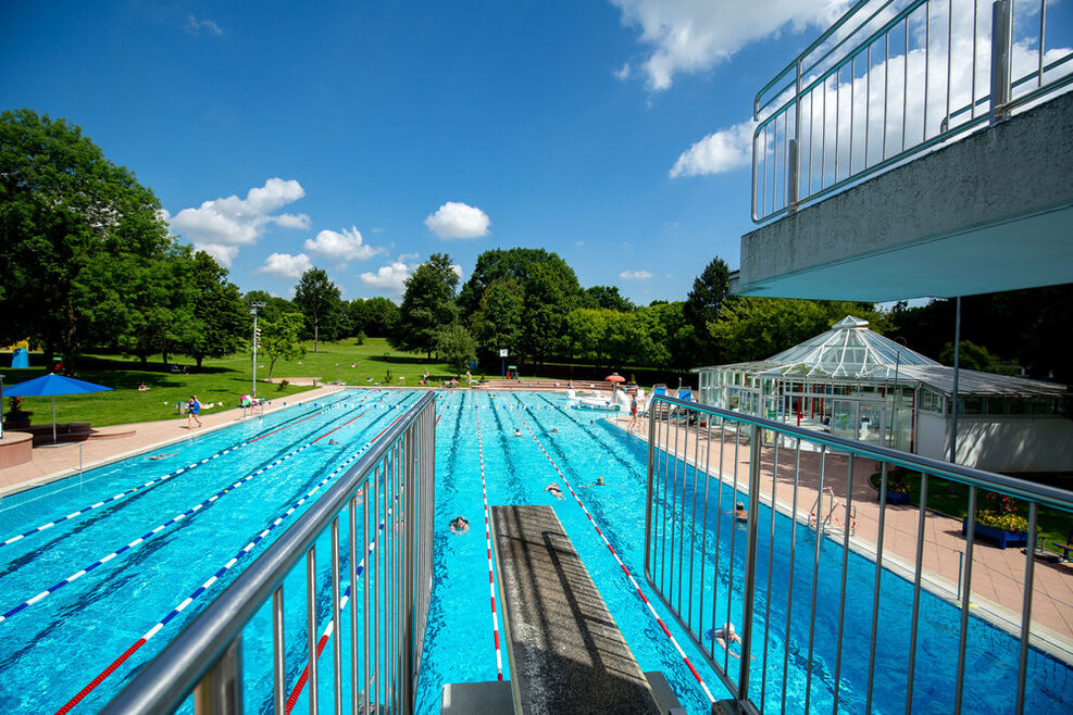 Das Außenbecken des Freibads Möhringen, mit einigen Schwimmern im Becken unter blauem Himmel.