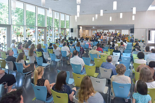 Publikum sitzt auf Stühlen in der neuen Mensa der Martin-Luther-Schule, auf der Bühne stehen Kinder und singen.