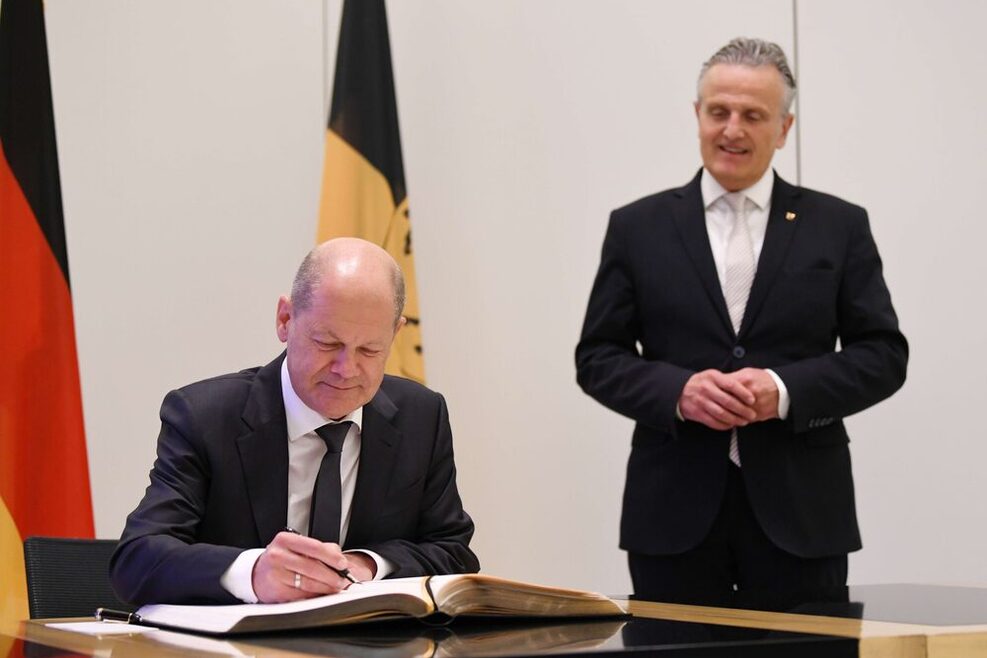 Der Bundeskanzler sitzt an einem Tisch und trägt sich in das Goldene Buch ein. Rechts neben dem Tisch steht Stuttgarts Oberbürgermeister.