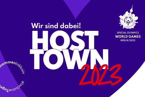 Das offizielle Logo des Host Town Programms der Special olympics World Games Berlin 2023. Zu sehen ist ein großes lilafarbenes Herz mit dem Schriftzug "Wir sind dabei! Host Town 2023"
