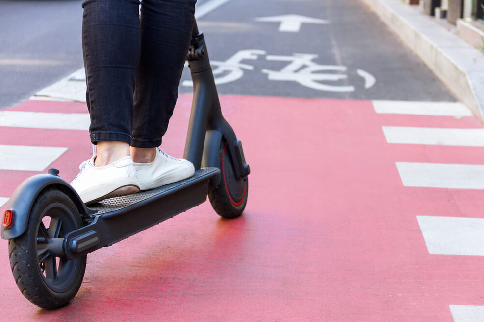 Junge Frau fährt E-Scooter auf dem Fahrradweg.