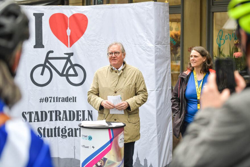 Bürgermeister Peter Pätzold gibt das Startsignal für Landeshauptstadt. Im Hintergrund ist ein weißes Banner, darauf visualisiert ist ein schwarzes Fahrrad, rotes Herz und der Stuttgarter Fernsehturm.