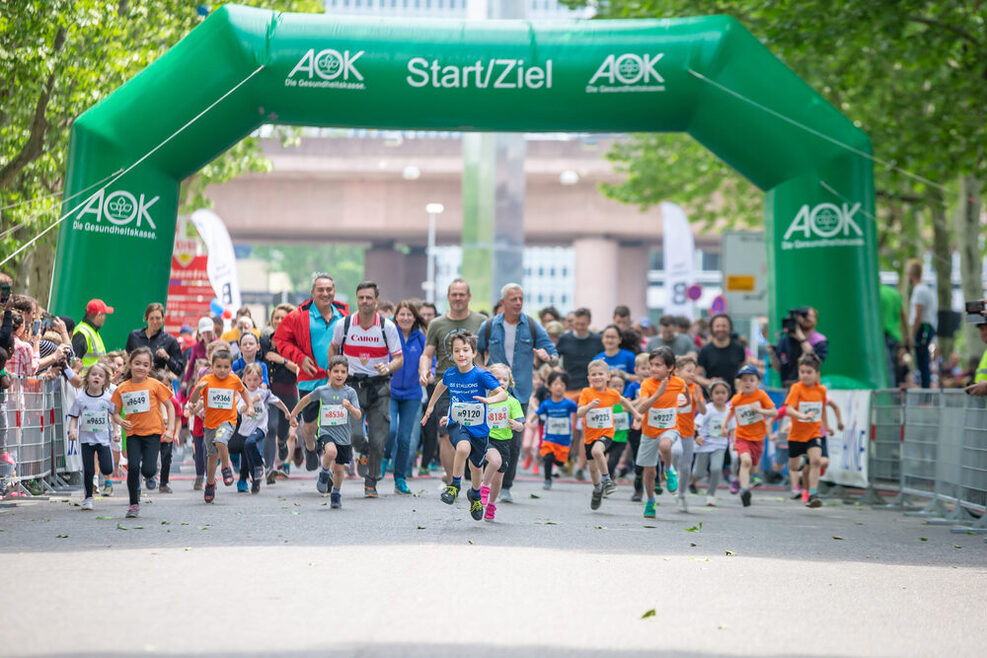 Ein Foto, dass beim Stuttgart-Lauf 2019 entstande ist. Zu sehen sind zahlreiche Kinder, die unter einem aufblasbaren Start und Ziel hindurch laufen.