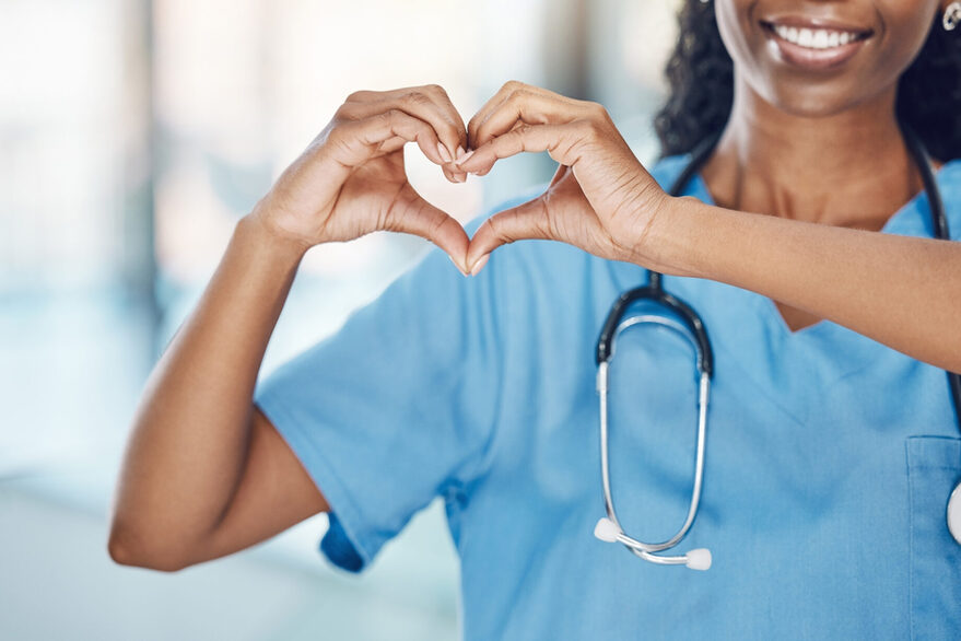 Eine Krankenschwester in Nahaufnahme formt mit ihren Händen und Fingern ein Herz.