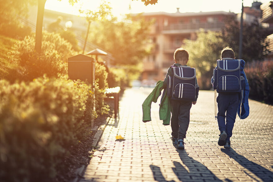 Zwei Jungen auf dem Heimweg von der Schule mit blauen Schulranzen.