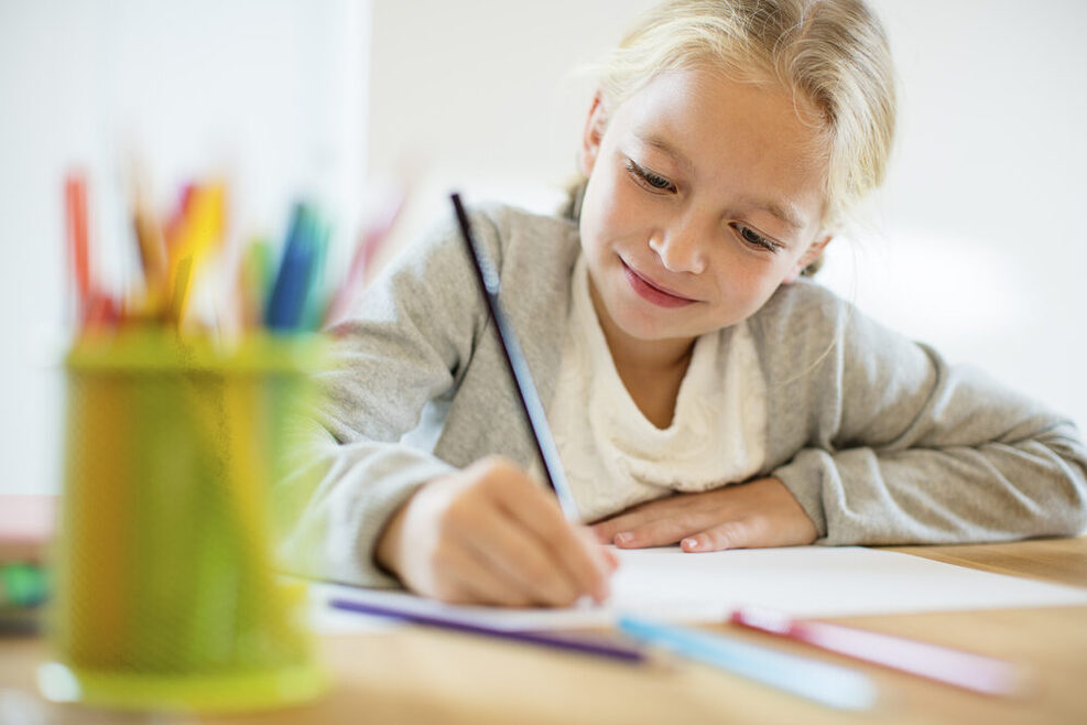 Ein Kind sitzt am Schreibtisch und malt