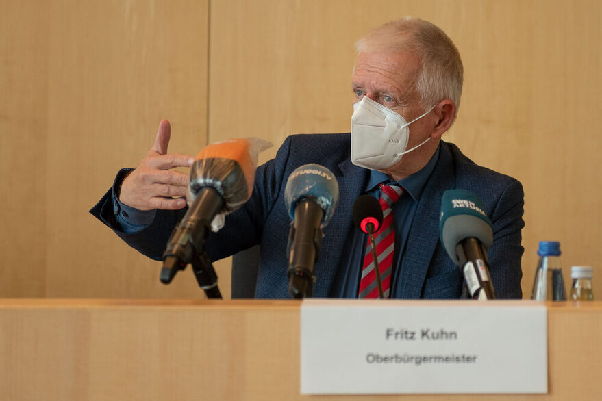 Oberbürgermeister Fritz Kuhn sitzt hinter einem Tisch mit Mikrofonen und erklärt das weitere Vorgehen der Stadt.