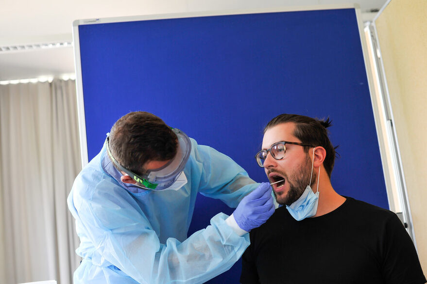 Mediziner nimmt bei einem Patienten einen Corona-Abstrich mit einem Wattestäbchen