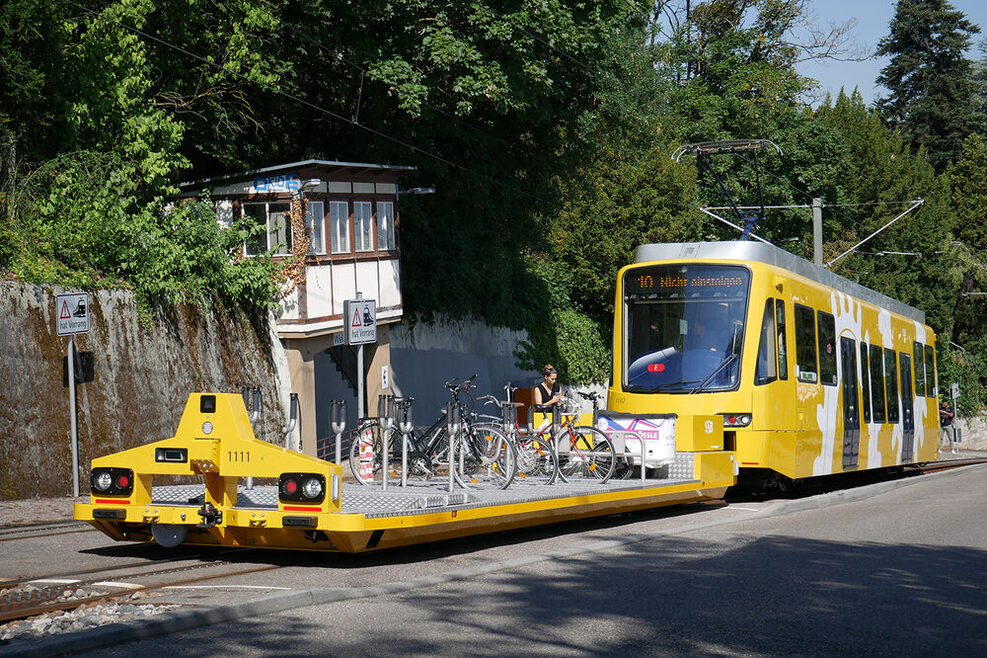 Der neue Triebwagen der Zahnradbahn "Zacke" fährt eine Anhöhe hinauf und schiebt eine Lore mit Fahrrädern vor sich her.