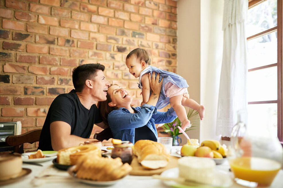 Mutter, Vater und Kleinkind sitzen gemeinsam an einem Frühstückstisch