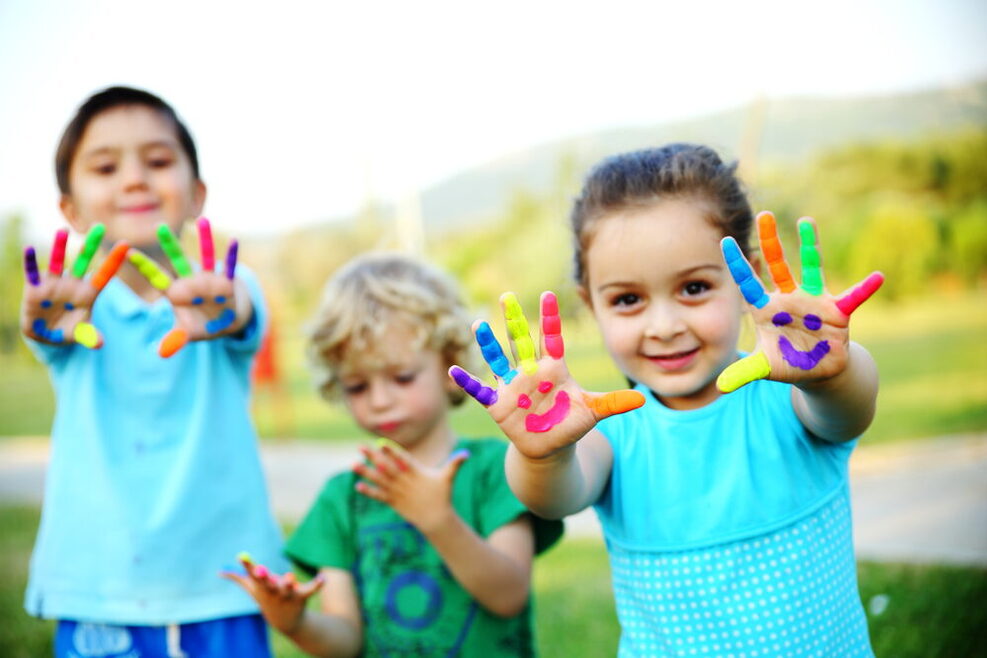 Ein Mädchen und zwei Jungen haben sich die Hände mit bunter Farbe bemalt.